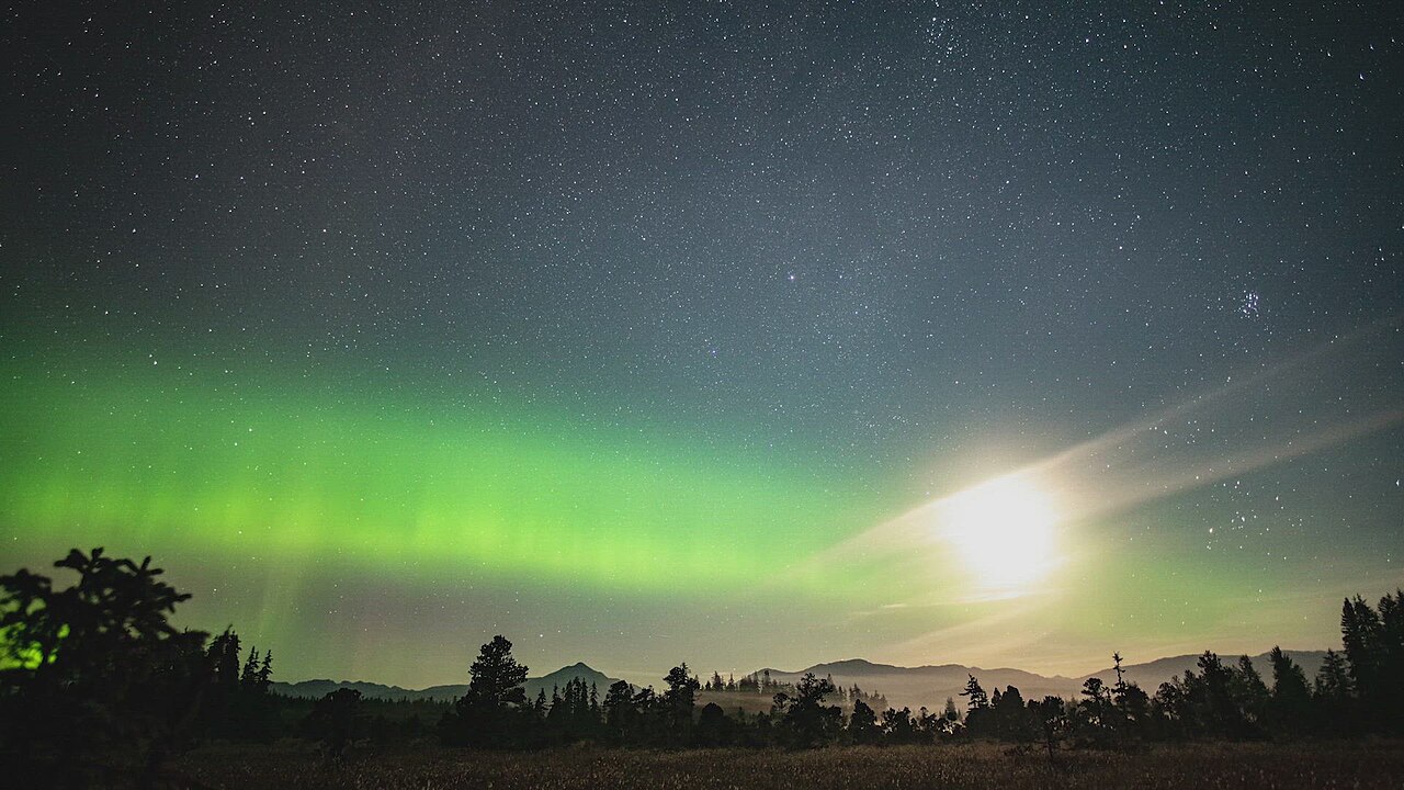Emerald green aurora sweeping across the night sky over Glacier Bay mountains